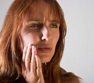 A woman hoping to visit a TMJ dentist appears to be in pain as she lightly touches the side of her jaw.